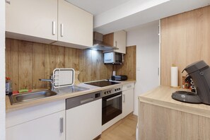 A compact kitchen with a microwave, oven, dishwasher, and a coffee machine.