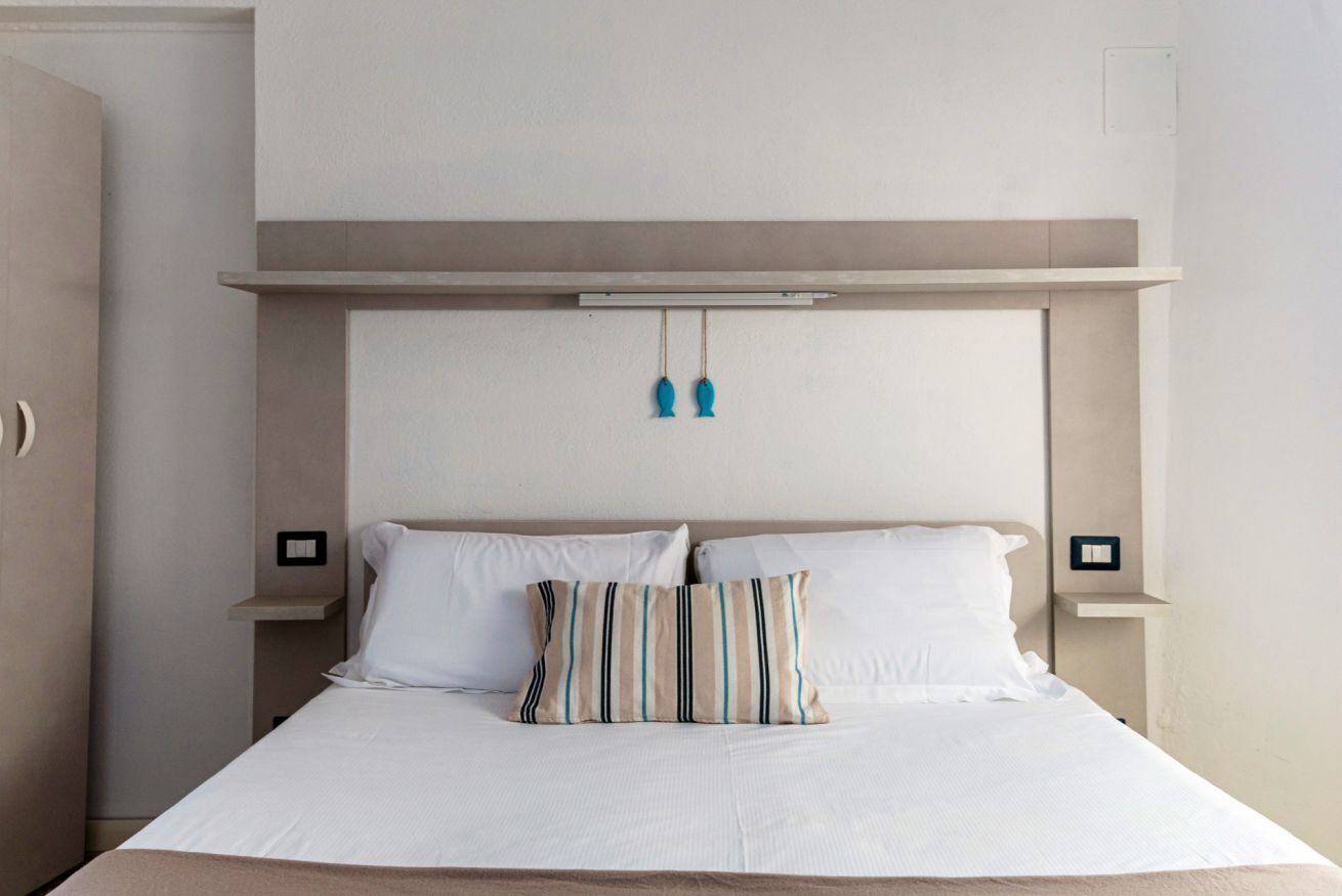 Uma cama com roupa de cama branca, um travesseiro listrado e uma cabeceira com luminária.