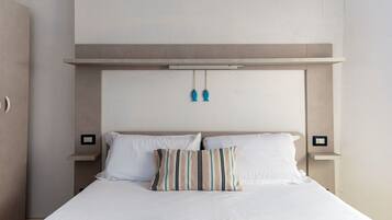 Uma cama com roupa de cama branca, um travesseiro listrado e uma cabeceira com luminária.