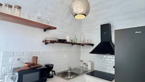 Una cucina con mobili bianchi, un frigorifero nero, un forno a microonde, un lavello e una lampada a sospensione.