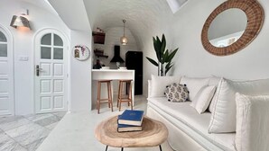 Un interno moderno con un divano bianco, un tavolo rotondo in legno con libri, uno specchio e un angolo cottura con sgabelli.