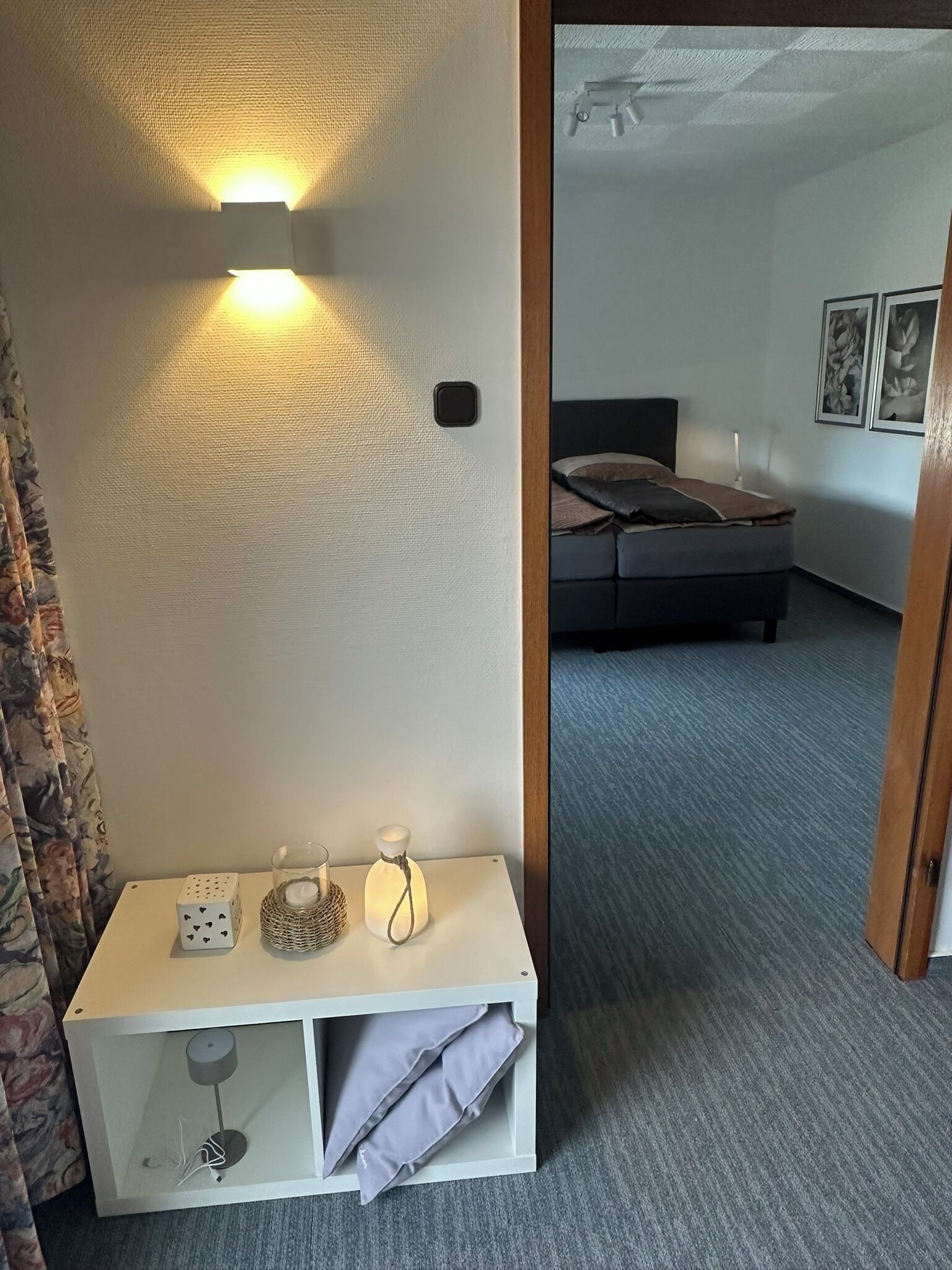 Ein Zimmer mit einem Bett, einem Nachttisch mit Lampe und einer Wandleuchte.