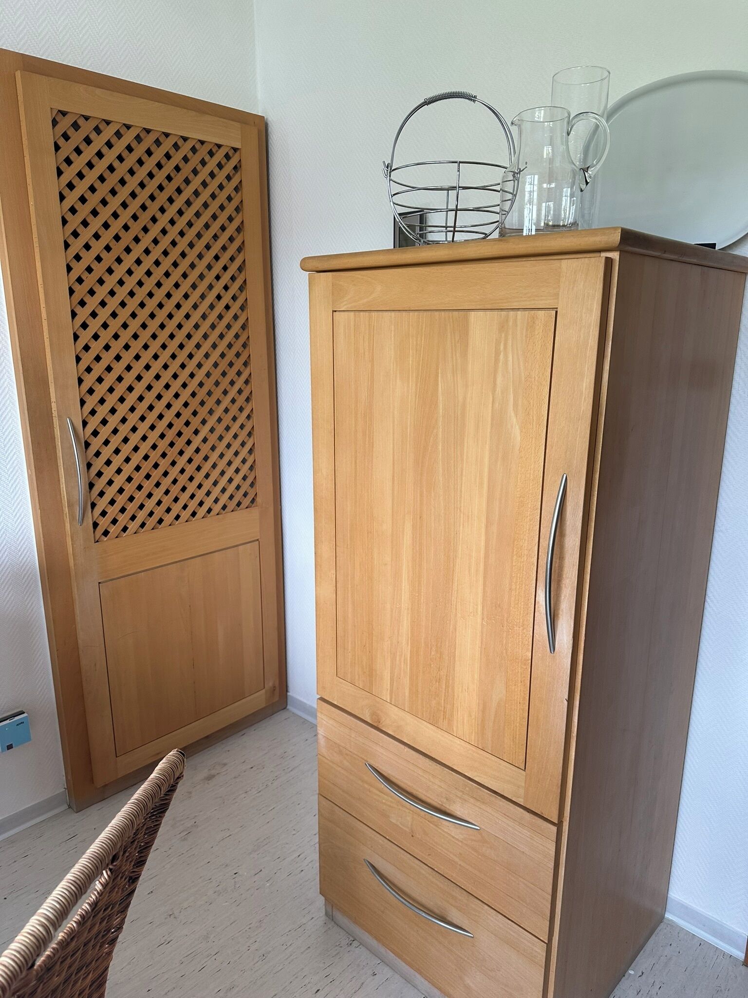 A wooden wardrobe with a lattice panel, two drawers, and a metal basket on top.