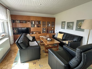 A living room with a sofa, a coffee table, a TV, and a bookshelf. - Geräumige Ferienwohnung Nähe Weser-Radweg, eigener Eingang (Bad Oeynhausen)
