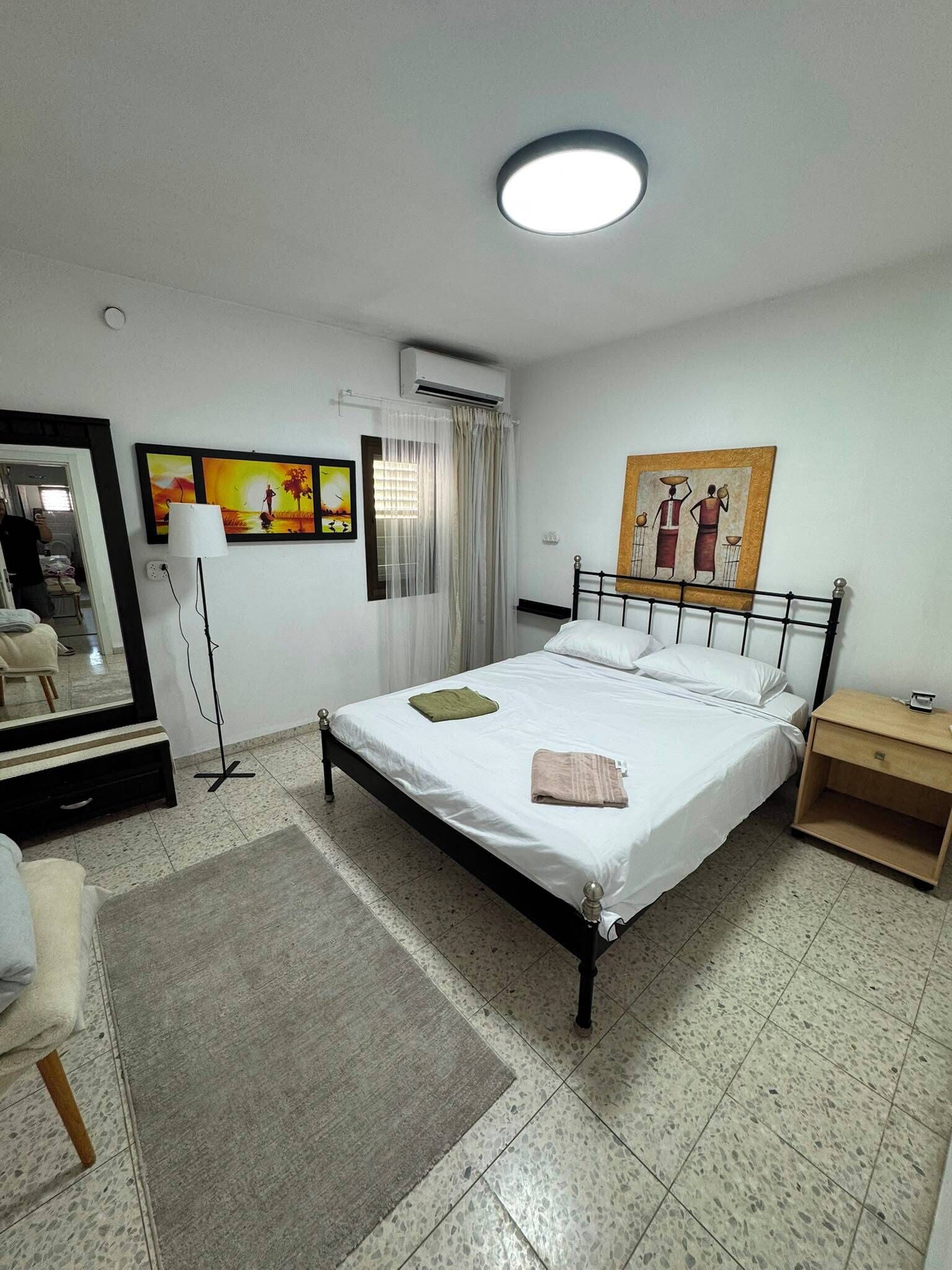 Una camera d'albergo con un letto, un comodino, una lampada, un quadro e uno specchio.