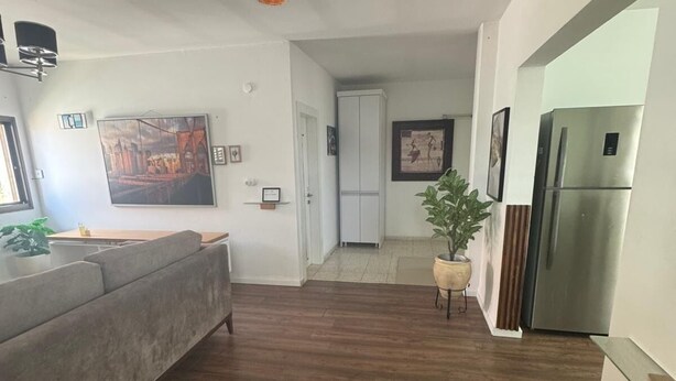 A modern kitchen with a grey sofa, wooden flooring, and a stainless steel refrigerator.