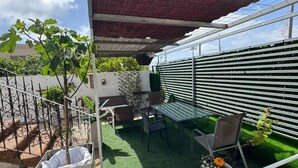 A covered patio area with a table and chairs, a hanging plant, and a white fence.