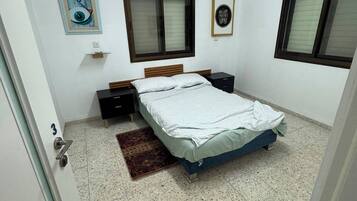 A bedroom with a bed, a nightstand, a wall-mounted air conditioner, a window, and a door.