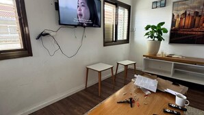 A modern living room with a wooden coffee table, a TV mounted on the wall, a potted plant, and a cityscape painting.