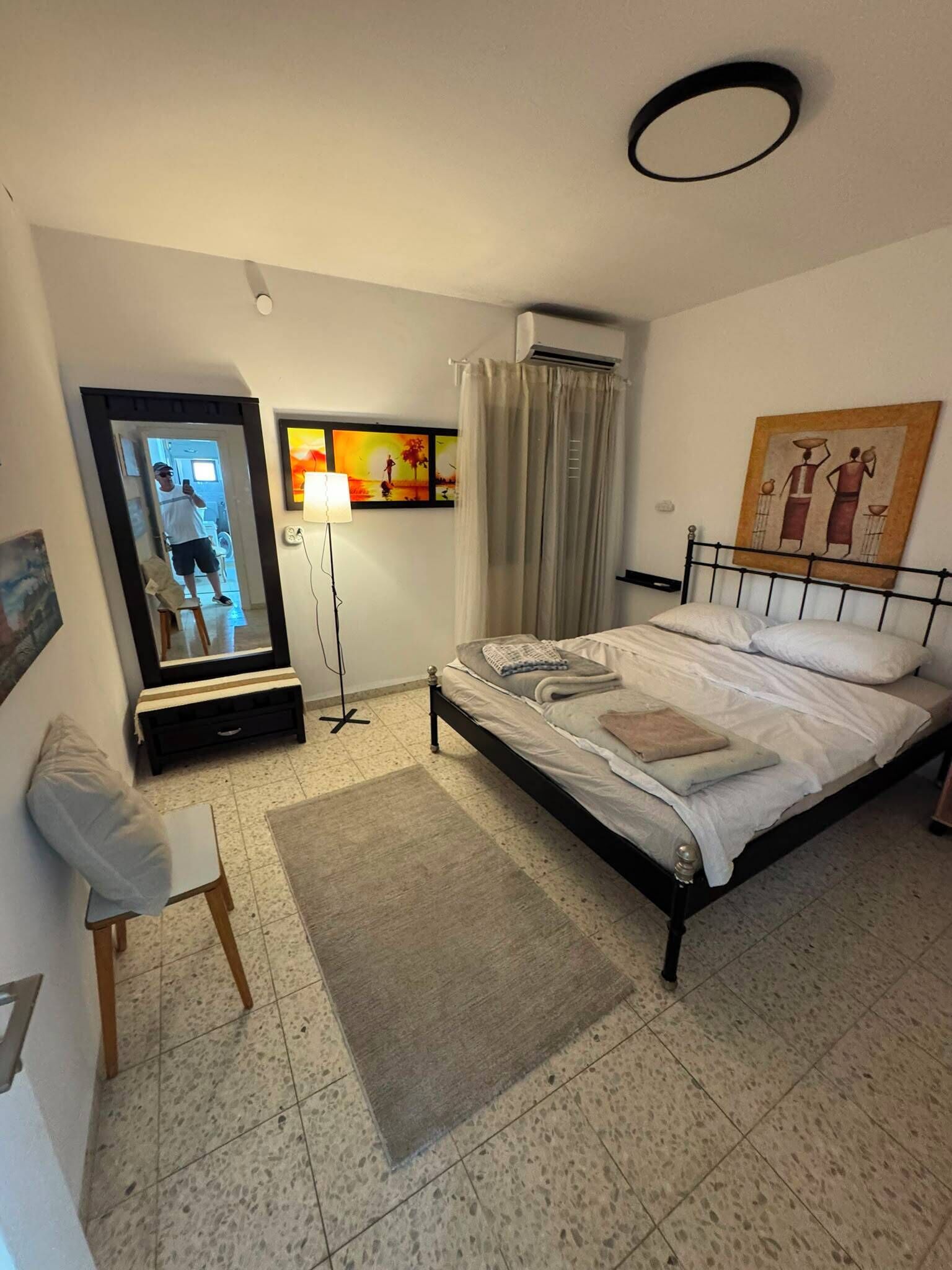 A hotel room with a bed, a desk, a chair, a floor lamp, and artwork on the walls.