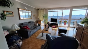 Una sala de estar con sofá, mesa de centro, televisor y ventanas amplias con vistas a la ciudad.