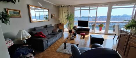 A living room with a sofa, coffee table, TV, and large windows offering a city view.