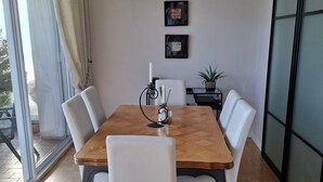 Un comedor con una mesa de madera, sillas blancas, una lámpara de araña y una puerta corredera de vidrio.