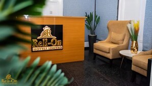 Un mostrador de recepción con un logotipo, una planta en maceta y dos sillones en el vestíbulo.