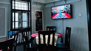 Un comedor con una mesa redonda, sillas, un televisor montado en la pared y un equipo de aire acondicionado.