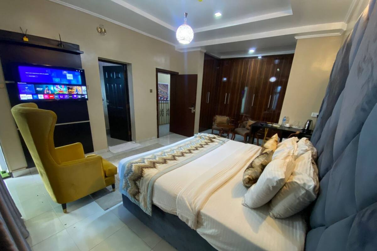 Ein modernes Schlafzimmer mit einem Bett, einem Fernseher, einem Sessel und einem Kleiderschrank.