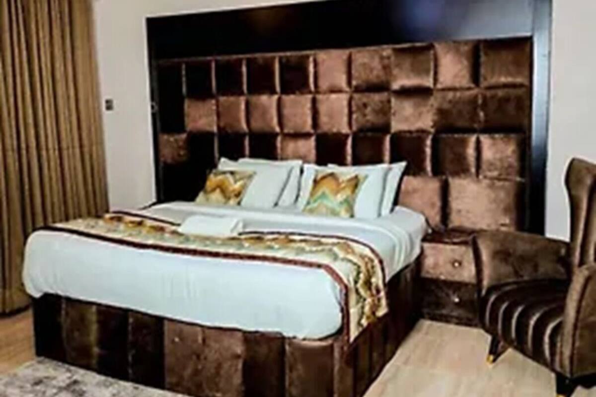 Ein Schlafzimmer mit einem großen Bett, einem dunklen Kopfteil, einem braunen Ledersessel und einem gemusterten Teppich.
