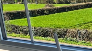 En vy från insidan av ett fordon, där man ser ut genom ett fönster mot en grön äng, en stenmur och ett slott på en kulle i fjärran.