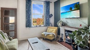Ett vardagsrum med en soffa, ett soffbord, en öppen spis, en tv och ett fönster med gardiner.