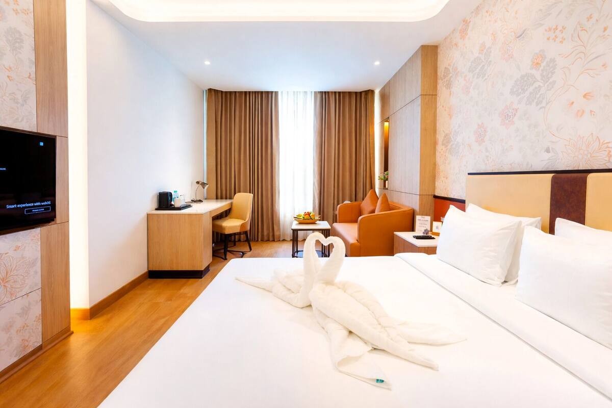 Habitación de hotel con cama, escritorio, silla, televisor y toalla con forma de cisne.