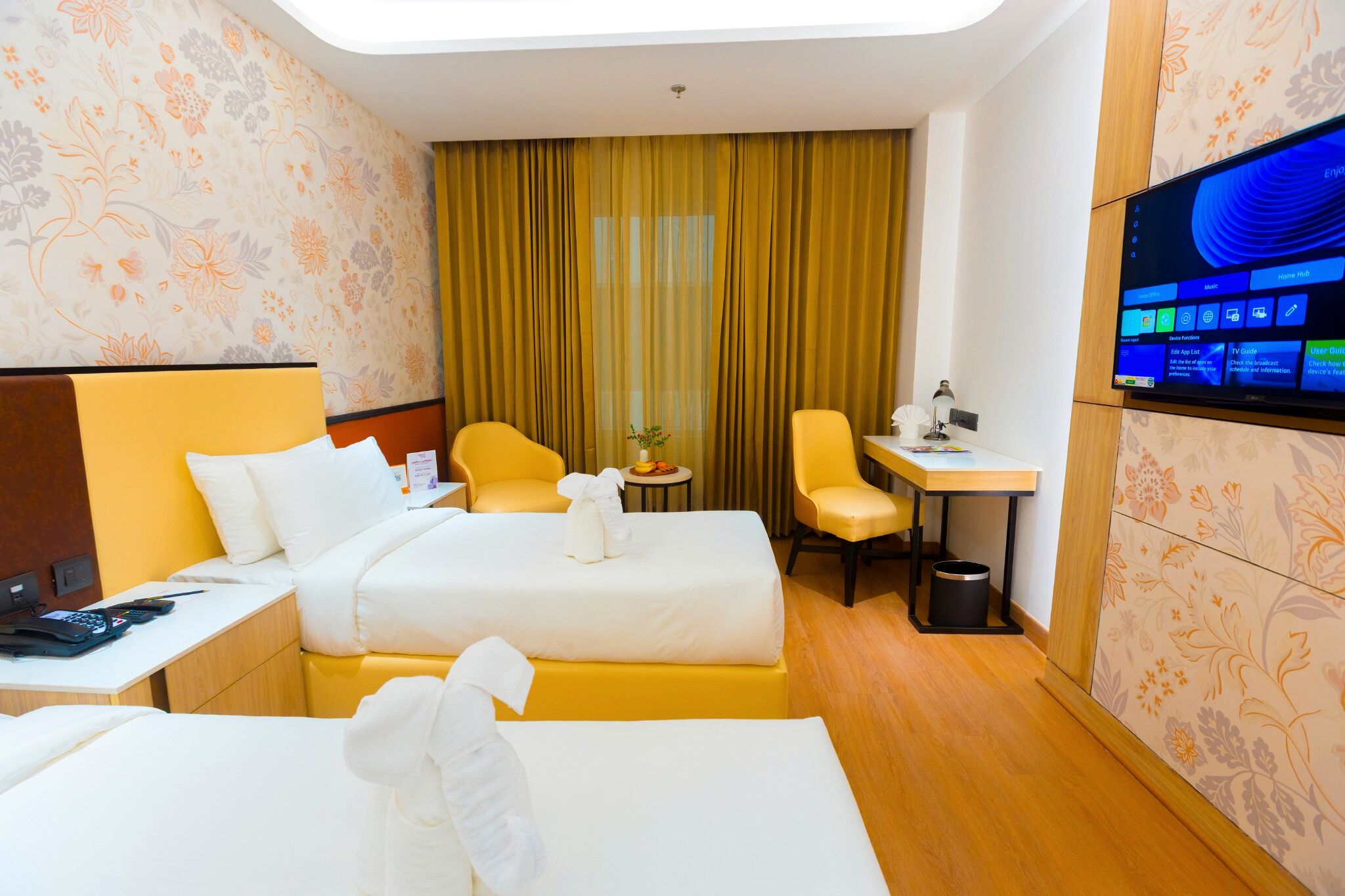 A hotel room with two beds, a desk, a chair, a TV, and a curtain.