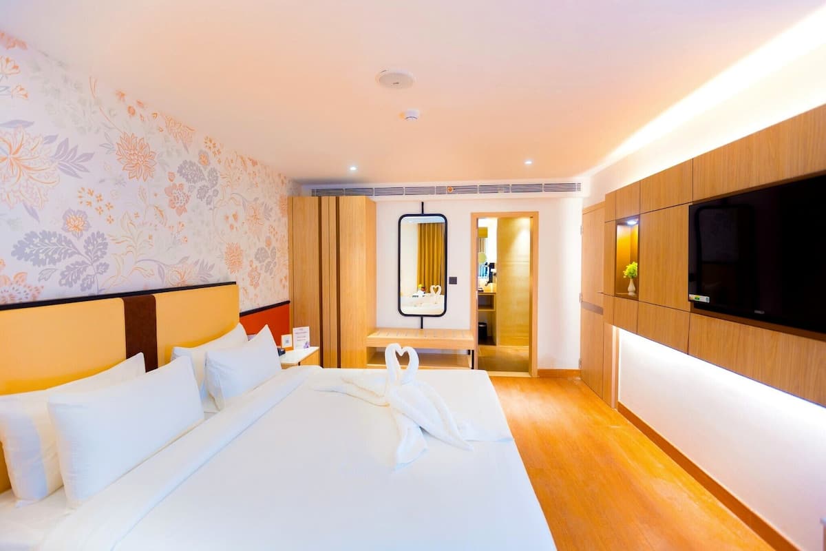 Una habitación de hotel con una cama, televisor, espejo y aparador de madera.