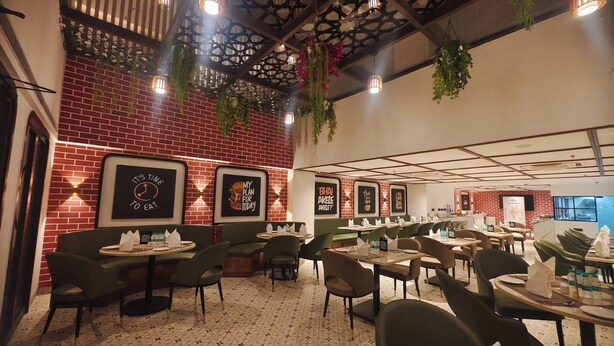 Un restaurant aux murs de briques, décoré d’affiches encadrées et de plantes suspendues. Les tables et les chaises sont disposées pour accueillir les clients.