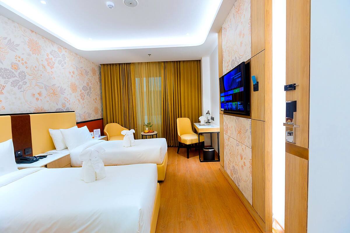 Habitación de hotel con dos camas, un escritorio, una silla, un televisor y una pequeña mesa con una planta.