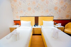 Une chambre d’hôtel avec deux lits, un plancher en bois, un papier peint à motifs floraux et une petite table sur laquelle se trouvent un téléphone et un panneau.