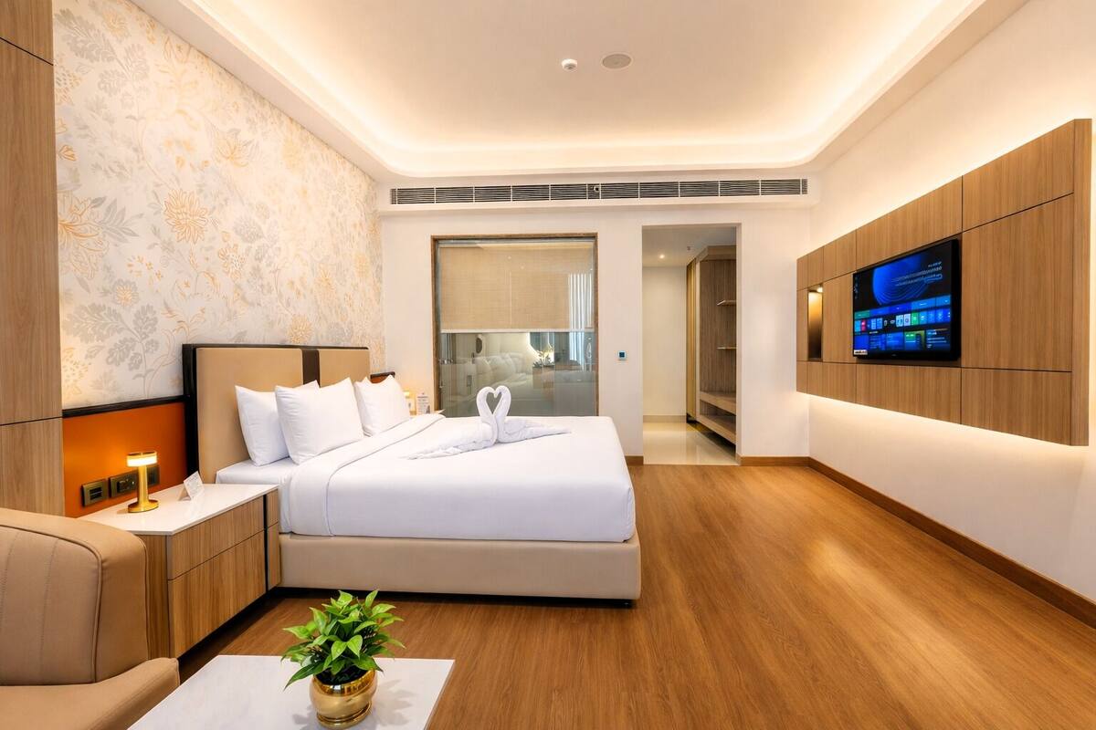 Una habitación de hotel moderna con una cama, mesita de noche, televisor y una planta en maceta.
