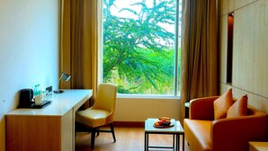 Une chambre d’hôtel équipée d’un bureau, d’une chaise, d’un canapé, d’une petite table et d’une fenêtre donnant sur la verdure.