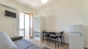 Uma sala de estar moderna com sofá, mesa de jantar com cadeiras, geladeira e TV na parede.