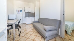 Um espaço compacto com cozinha compacta, um sofá, uma mesa de jantar com cadeiras e uma cama com colcha listrada.