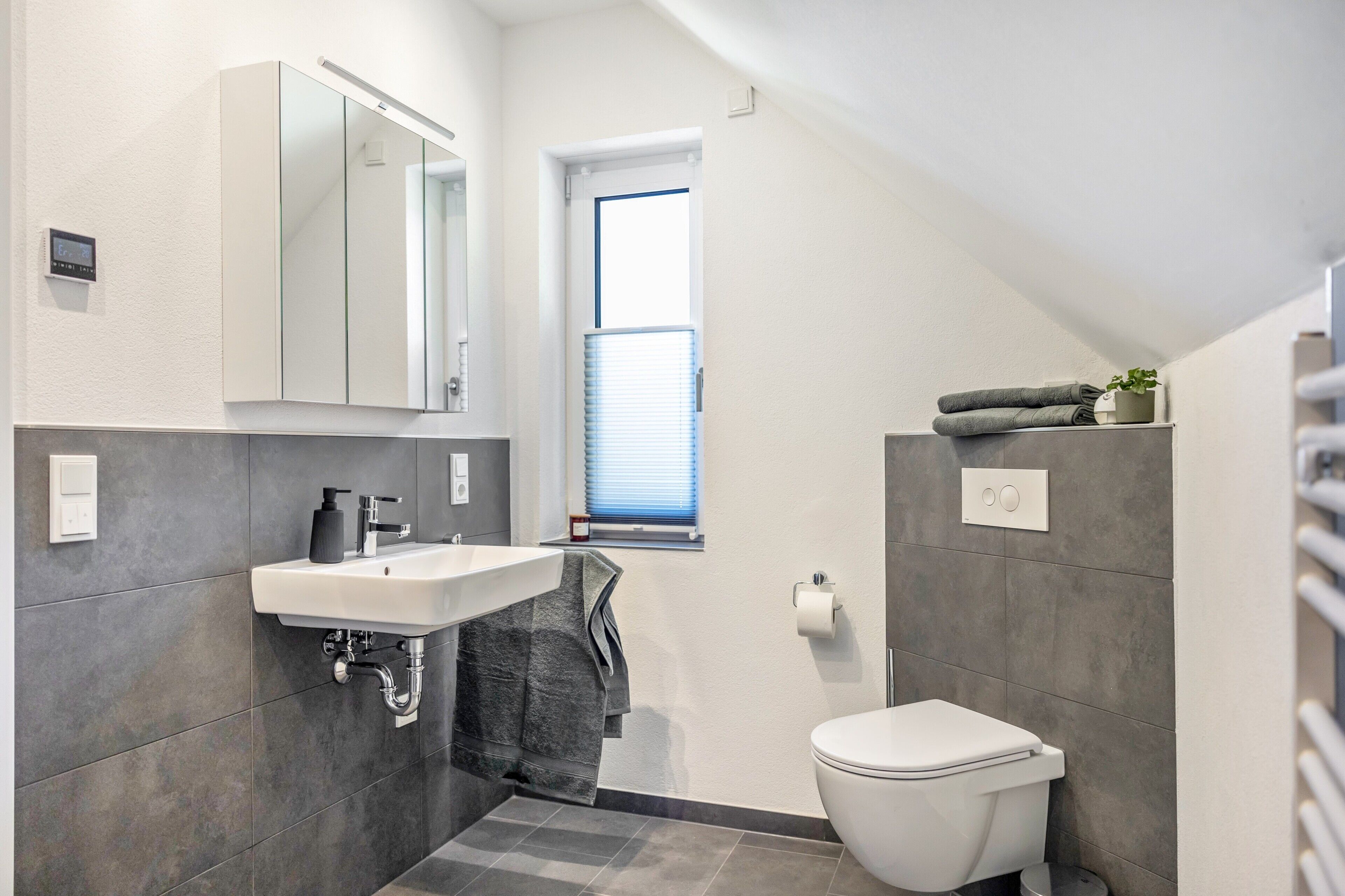 Une salle de bain moderne avec un lavabo blanc, un miroir, des toilettes et une fenêtre.