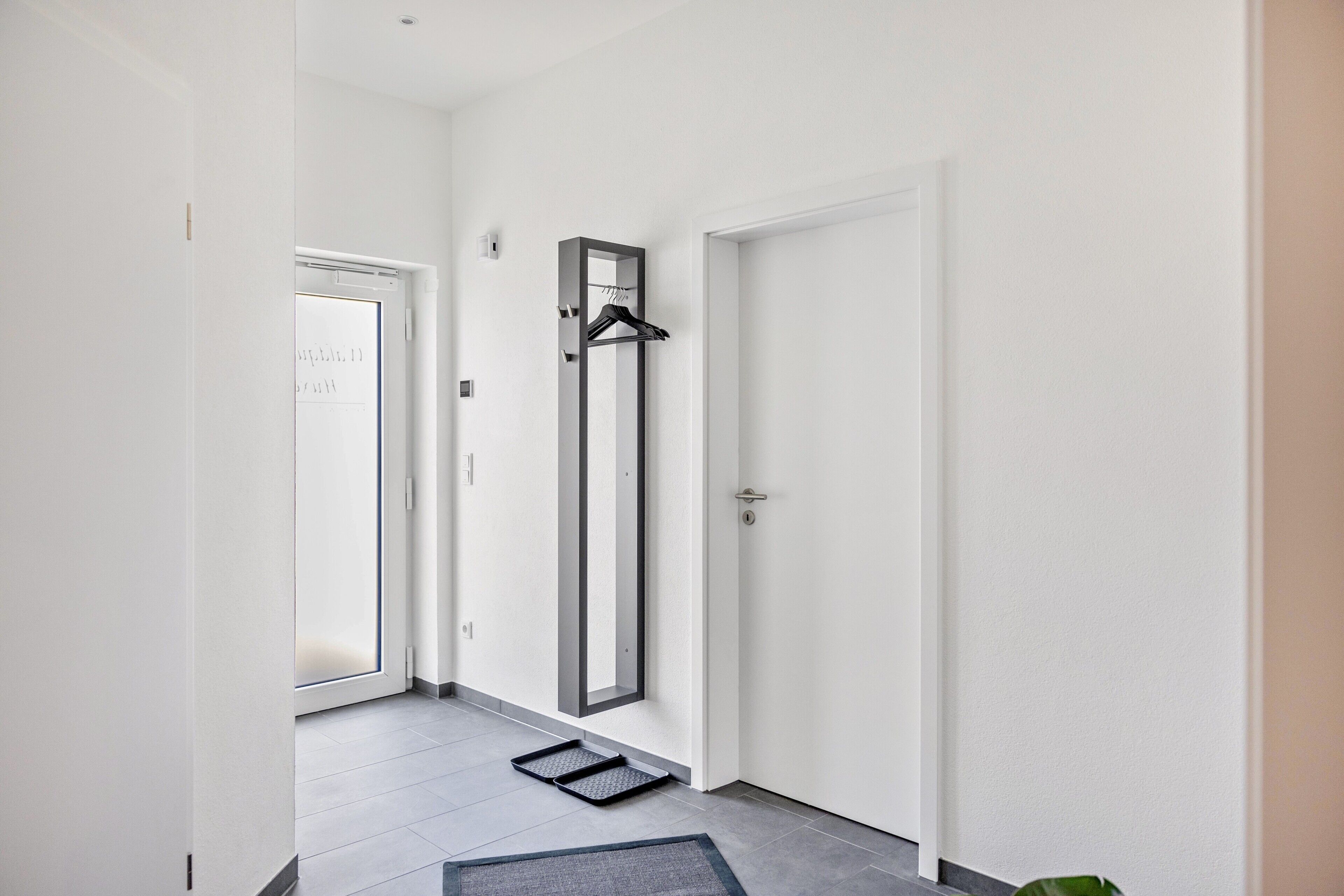Un couloir avec une porte, un porte-manteau et un paillasson sur le sol.