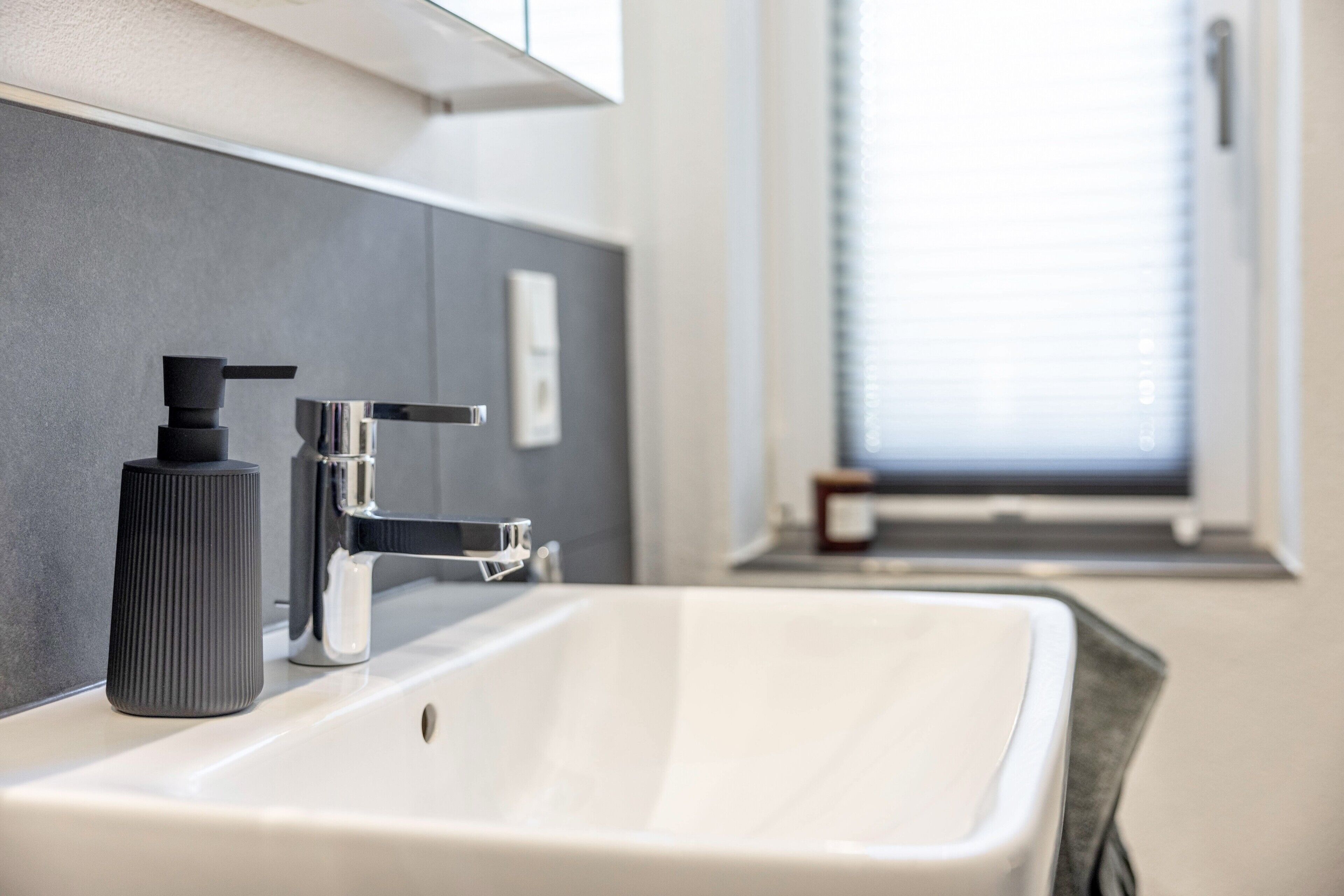 Een moderne badkamer met een wit wastafel, een zwarte zeepdispenser en een chromen kraan.