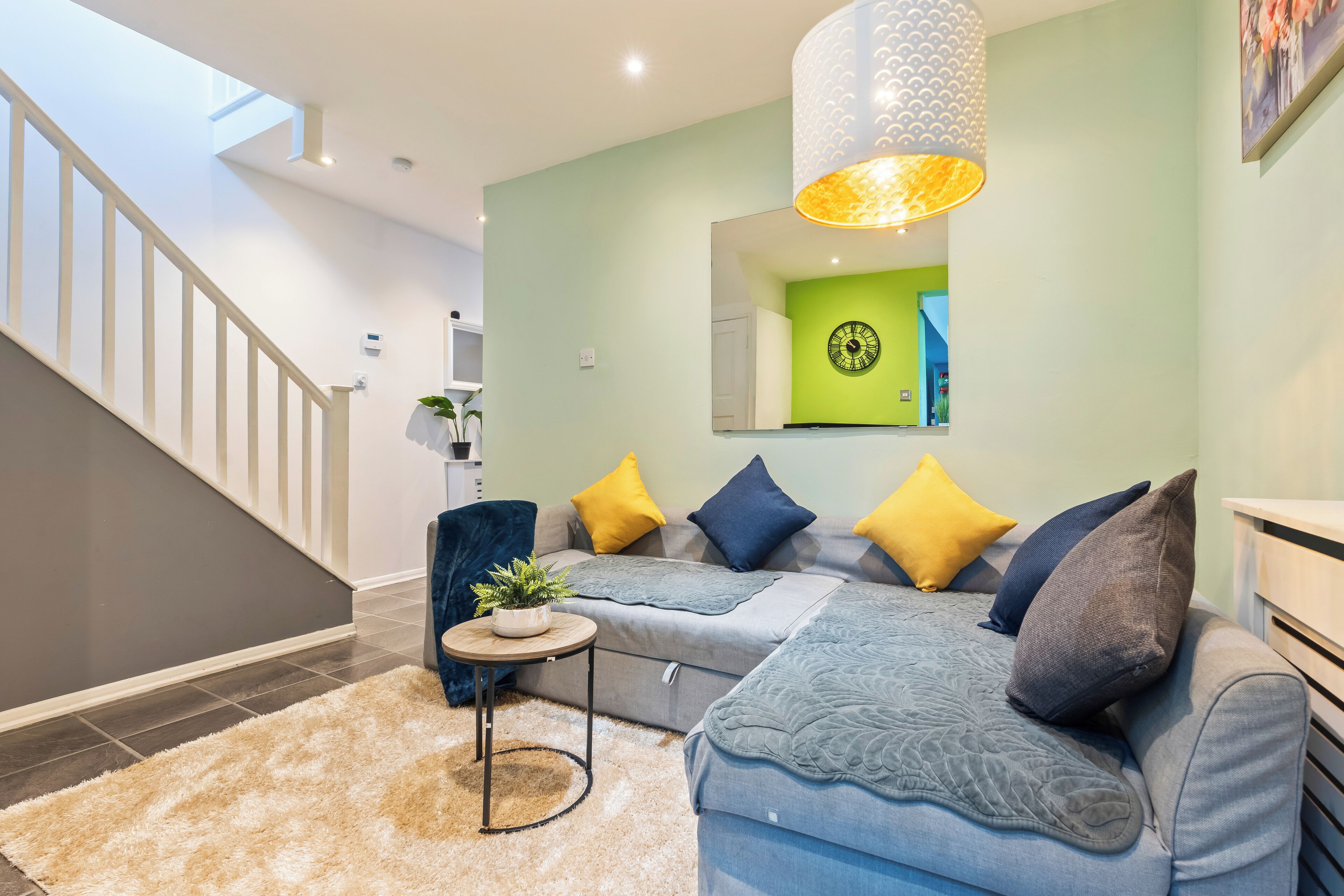 A modern living room with a staircase, a sofa set, a small round table with a plant, and a large pendant light.