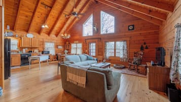 A log cabin interior with a dining area, kitchen, and a large sofa.