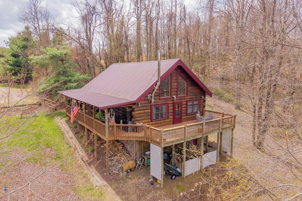 Charming log cabin with a spacious wraparound deck in a peaceful wooded setting.