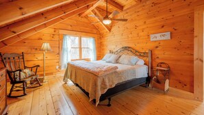 Une chambre dans une cabane en bois, avec un lit, un fauteuil à bascule et un ventilateur de plafond.