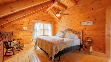A wooden cabin bedroom with a bed, rocking chair, and a ceiling fan.