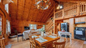L’intérieur d’une cabane en bois comprend un coin repas, une cuisine et un escalier menant à un niveau supérieur.