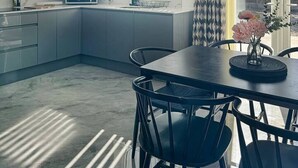 Une cuisine moderne dotée d’une verrière, d’un coin repas avec une table et des chaises, et d’une fenêtre avec des stores verticaux.