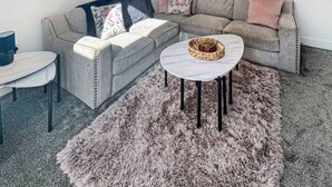 Un salon moderne avec un canapé d’angle, une table basse ronde, un tapis moelleux et des éléments de décoration fixés au mur.