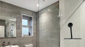 Ein modernes Badezimmer mit Duschkabine aus Glas, Toilette, Waschbecken und Spiegel.