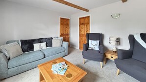 Een woonkamer met een blauwe bank, twee fauteuils, een houten salontafel en een lamp.