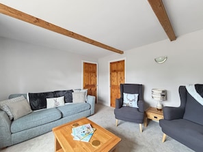 Ein Wohnzimmer mit einem blauen Sofa, zwei Sesseln, einem Holztisch und einer Lampe.
