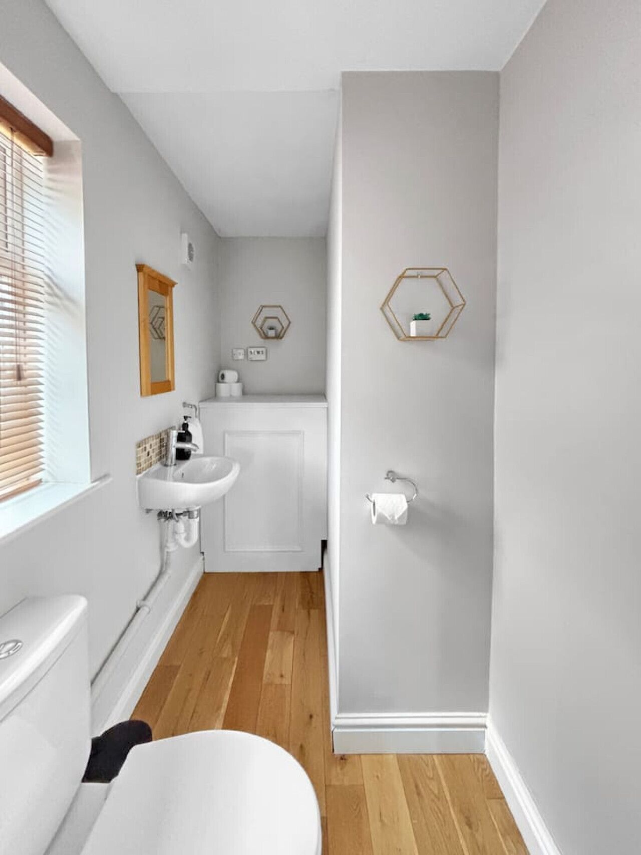 A bathroom with a toilet, sink, and shower area. There are wooden blinds on the window, and a towel rack is visible.