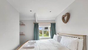 Een slaapkamer met een bed, een raam met gordijnen, een wandlamp en een houten hoofdbord.
