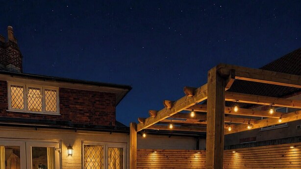 Een houten kuubbad buiten met een pergola, een bakstenen huis op de achtergrond en een grindpad.